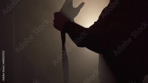 Cropped view of boxer wrapping his hands with white bandages in dark smoke background. photo