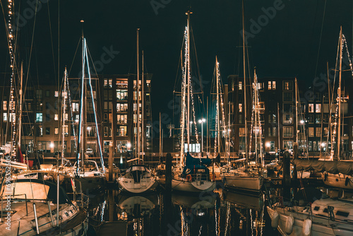 The Hague, Netherlands - January 1, 2020: Scenic panorama of Scheveningen harbour. Romantic modern seaside resort. Brown brick buildings, light windows, moored white yachts and sailboats in evening. photo