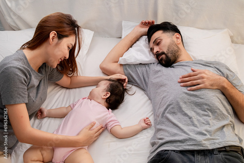 Cute infant girl sleep in mother arm feeling warm safe in bed after tired playing together, Multicultural family happy relationship spend great time nurturing baby daughter with love and care bonding