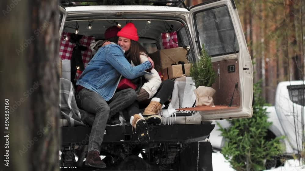 A Young couple is sitting in a trunk of retro car with holiday's brights in background. New Year's gifts, plaid. girl, happiness, Christmas celebration, holiday. A Young couple is sitting in a trunk of retro car with holiday's brights in background. New Year's gifts, plaid. girl, happiness, Christmas celebration, holiday.