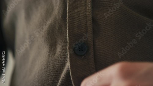 Stab macro closeup of hands buttoning up brown shirt made from close fabric while getting dressed indoors photo