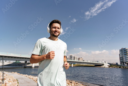 A man with headphones music for a runner workout warm-up jogging in sports clothes and a T-shirt. Uses a fitness watch on his arm and a sports app.