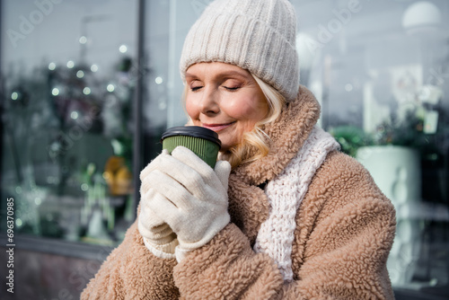 Photo of shiny cute woman wear beige coat closed eyes enjoying hot coffee aroma smiling outside urban city street © deagreez