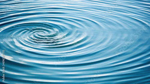 Water drop close up with ripples on blue water surface background.