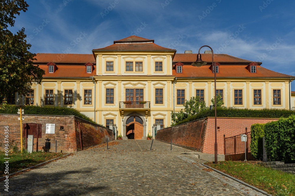 Svojsin, Czech Republic - October 13 2023: Front view of the newly renovated castle, a yellow building with red roof, cobble stone paving and red brick walls. Sunny autumn day with blue sky.