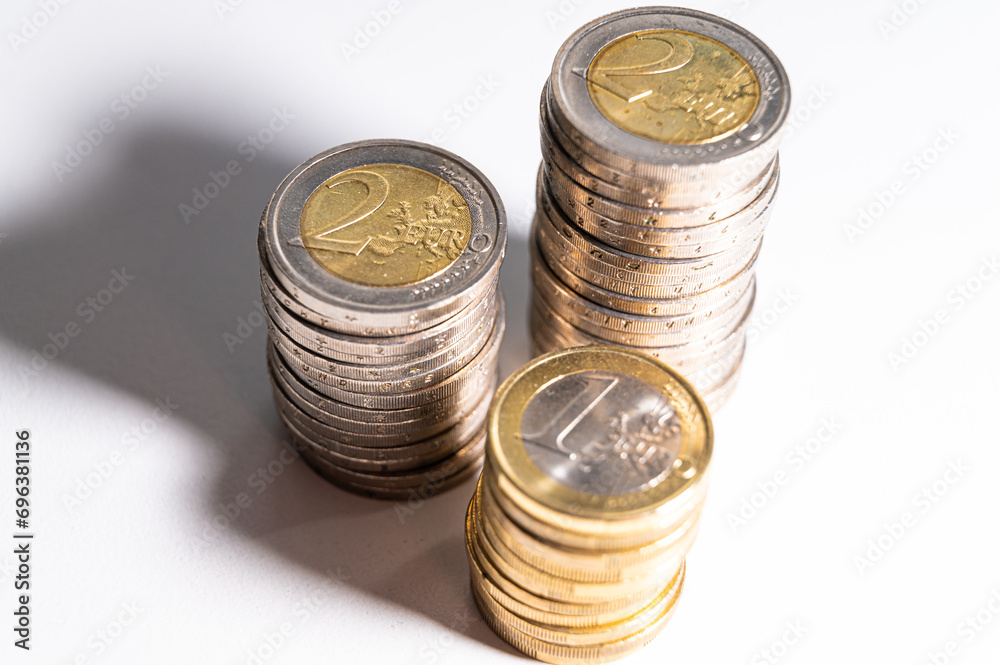 Stacks of coins next to each other, on white surface, and their shadows. Quantity of money, currency and wealth. Stacks of coins next to each other, on white surface, and their shadows. Quantity of money, currency and wealth.