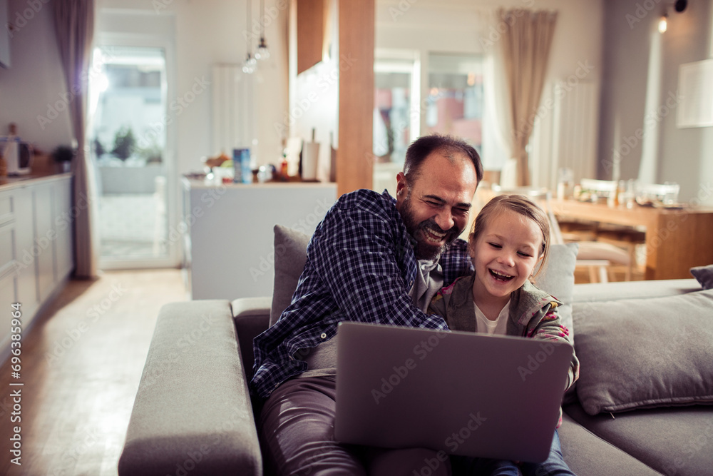 Happy little girl sitting on couch with father using laptop Happy little girl sitting on couch with father using laptop