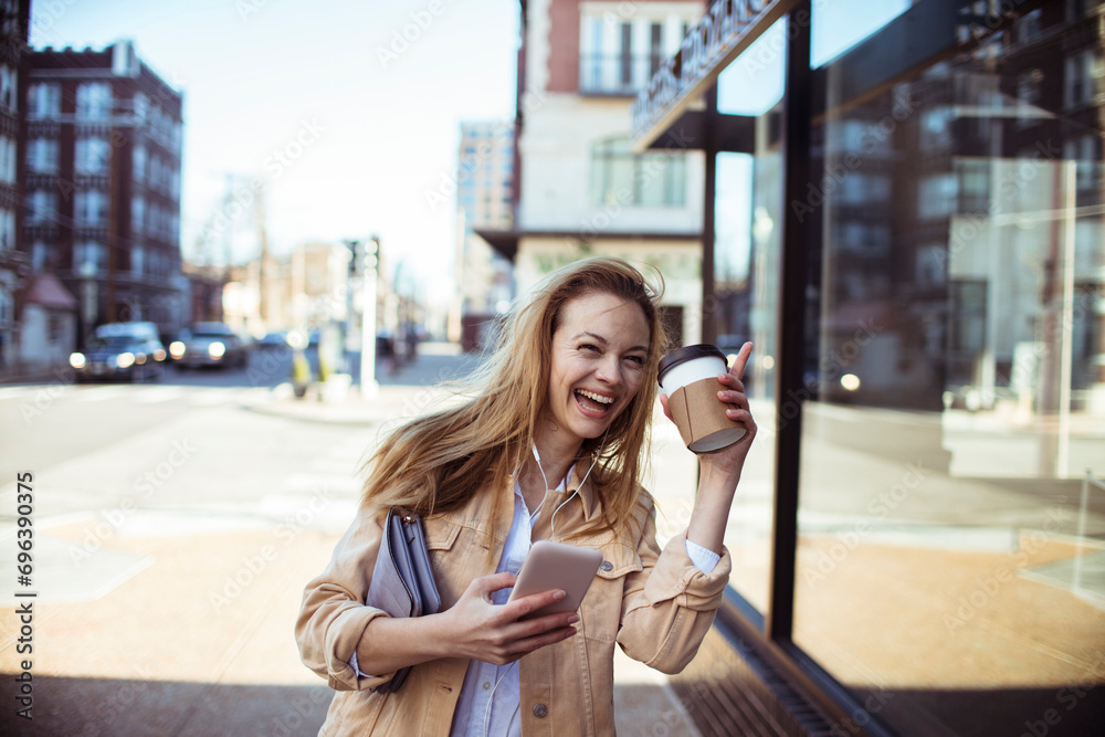 Woman enjoying her coffee and smartphone with earphones while walking on a sunny city street