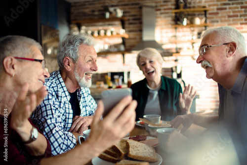 Group of senior friends enjoying a meal together while using smartphone at home