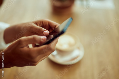 Close-up of a female hands, using a mobile phone, a cup of coffee in the background. photo
