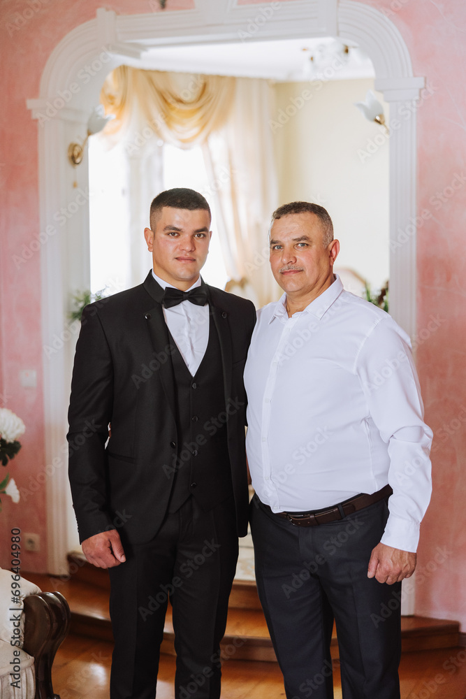 A father hugs his mature son and helps him prepare for the wedding ceremony. Warm and sincere relations between a father and an adult son. An emotional moment at a wedding