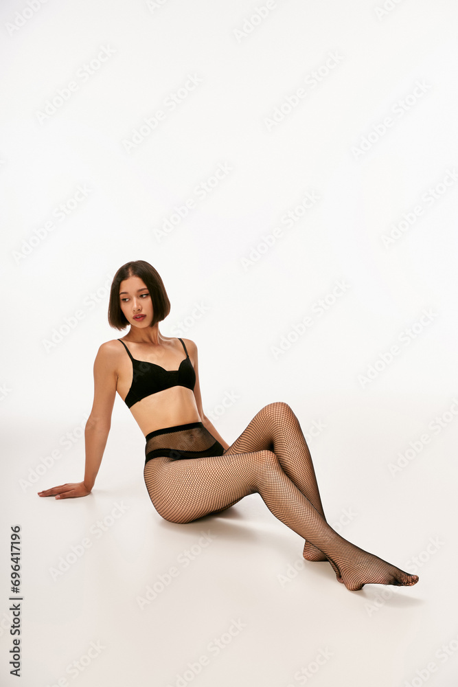 beautiful and young asian woman in black underwear and fishnet tights posing on white background