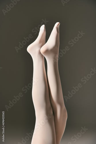 cropped view of young woman in white pantyhose posing with raised legs on dark grey background
