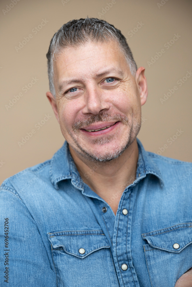 Obraz premium cool man, 46 age, with grey hair, blue jeans, blue shirt, posing in front of brown studio, portrait, concept, business, casual