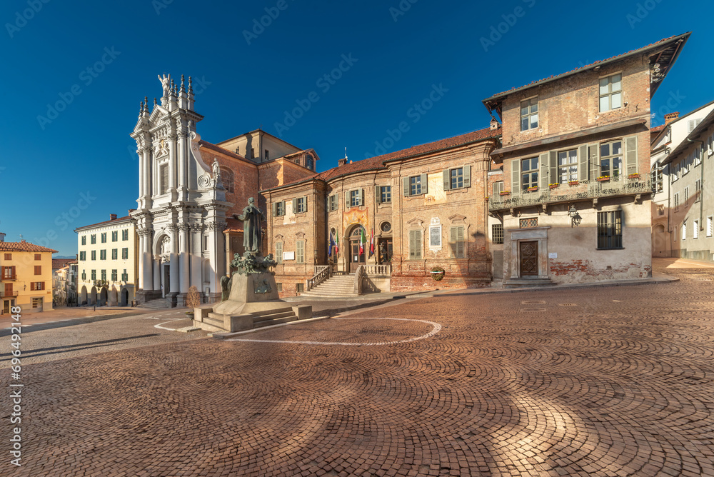 Bra, Cuneo, Italy - The town hall and parish church Sant' Andrea Apostolo in Piazza Caduti per la Liberta, Coblestone with the statue of St. Joseph Cottolengo