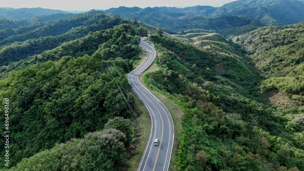 Aerial view highway Drone flying above winding road during sunlight, Winding asphalt road through tropical rainforest. countryside landscape. Landmark tourist attractions in Nan Province, Thailand.	
