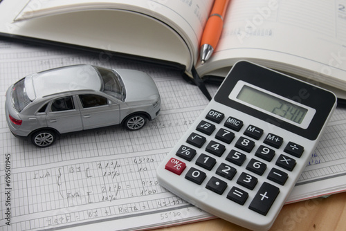 Close-up of a calculator next to a car and a notepad with notes on tax costs