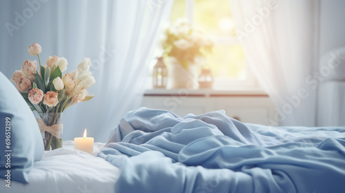 Cozy light white Bedroom with flowers and candles. pillows, duvet on a bed. Blue bed linen on a blue sofa. Bedroom with bed and bedding. Blurred view of light bedroom with big window