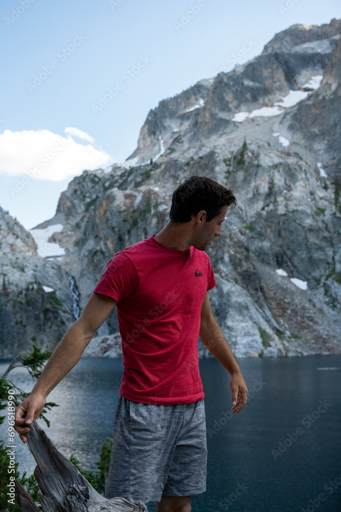 Naklejka premium Portrait of man in red shirt in front of Goat Lake in Sawtooth Mountains in Idaho, USA. Beautiful rugged mountain range in western United States. Located near Stanley, Idaho.