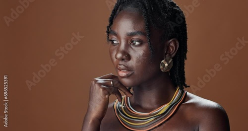 Face of black woman, skincare or model thinking of wellness, necklace or healthy beauty in studio. Dermatology, dreadlocks or African person with glow, idea or natural aesthetic on brown background photo