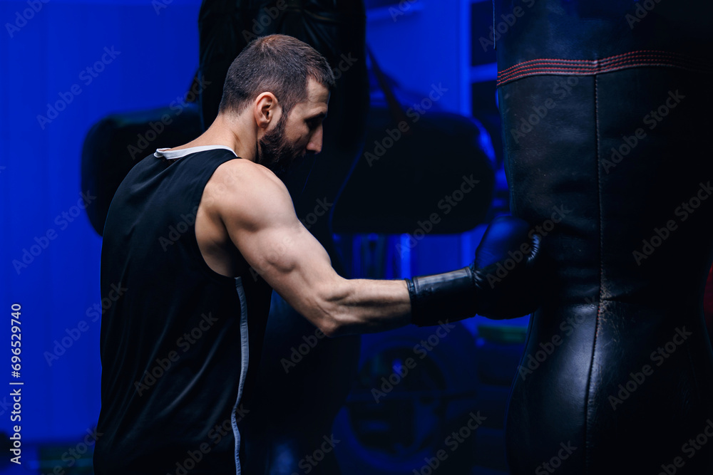Male boxer trains punches on punching bag, dark background