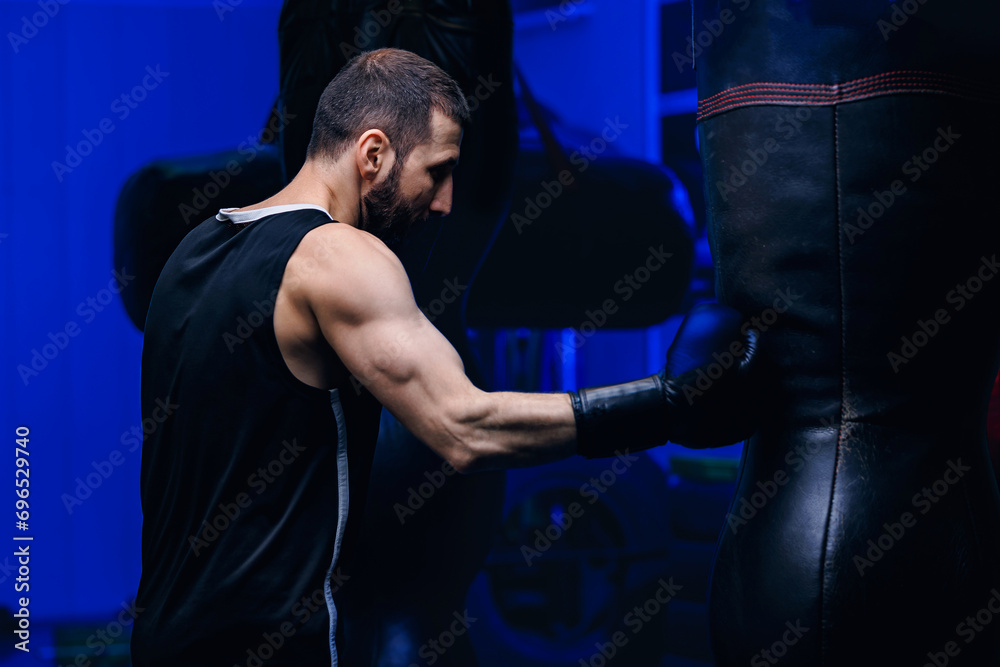 Male boxer trains punches on punching bag, dark background Male boxer trains punches on punching bag, dark background