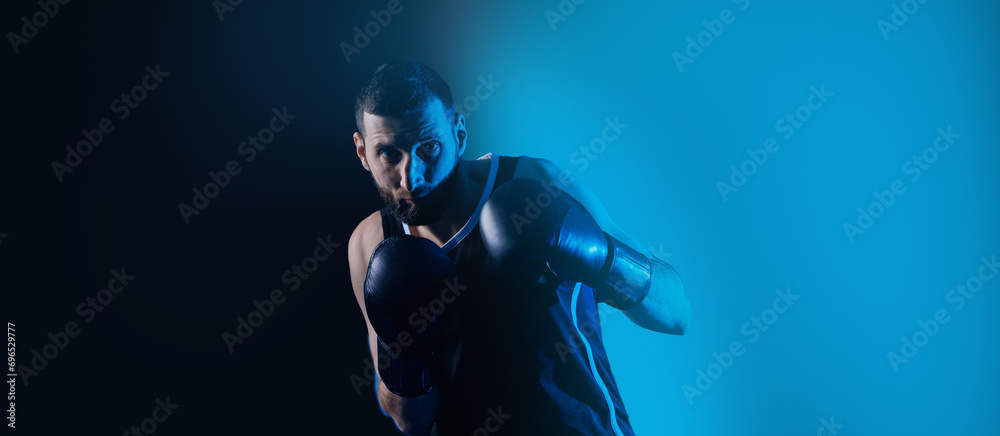 Male boxer trains punches on punching bag, dark background neon color. Concept banner sport boxing