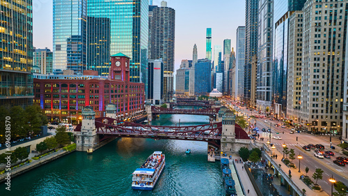 Chicago boat going under canal bridge aerial with city lights and skyscrapers at blue hour, tourism photo