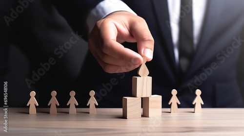 A businessperson's hand selects a wooden figurine chess from the table and places it on a elevated platform made of wooden blocks at the center of the table.Talent selection, recruitment concept