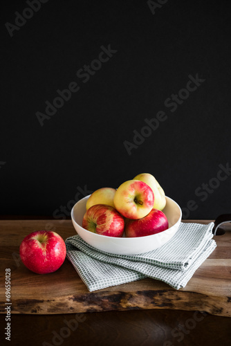 Fresh healthy red and yellow apples in white bowl with kitchen towel on wooden table cutting board with dark background room for copy