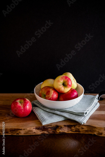 Fresh healthy red and yellow apples in white bowl with kitchen towel on wooden table cutting board with dark background room for copy
