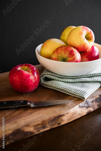 Fresh healthy red and yellow apples in white bowl with kitchen towel on wooden table cutting board with dark background room for copy