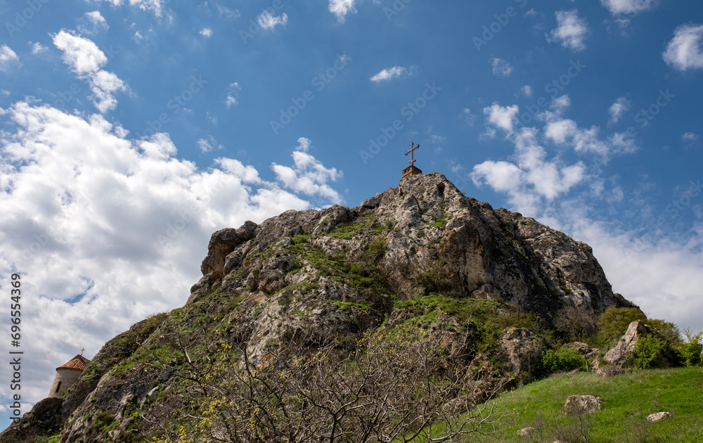 Metal Orthodox cross on top of rock, blue sky background. Religious symbol