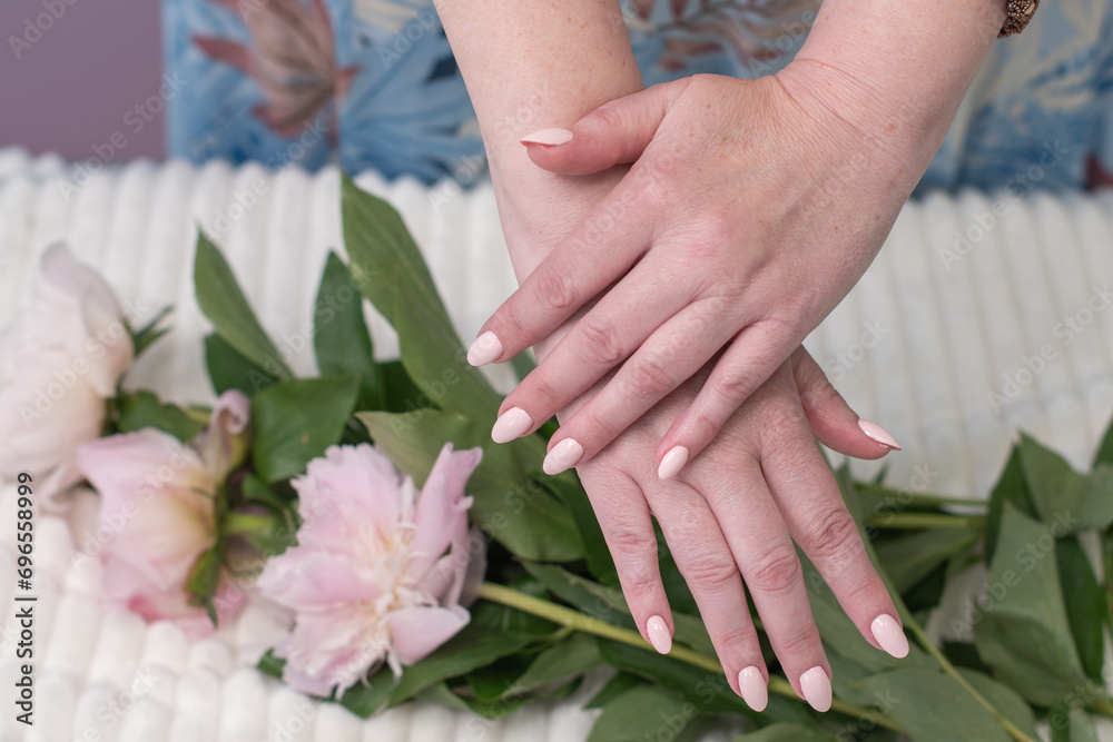 Fototapeta premium female hands with a beautiful peach manicure design, color 2024, pastel colors, delicate spring dewy peonies in the hands of a model, high quality photo