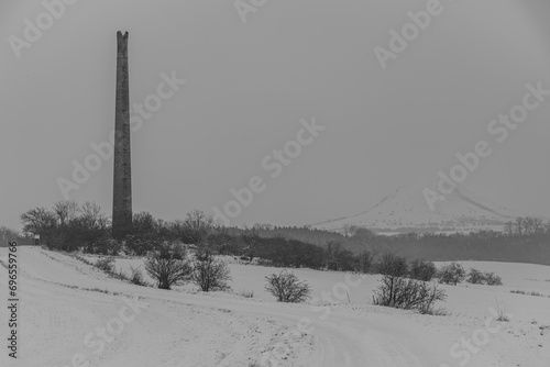 Rana hill in white storm snowy morning near Louny town with ruin chimney photo