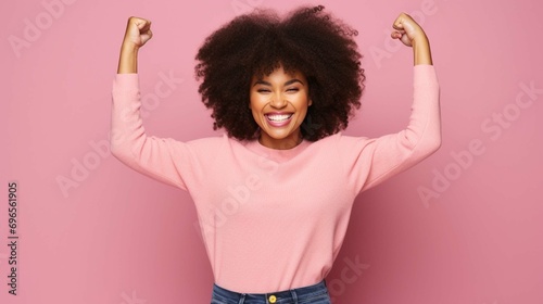 Self assured beautiful young Afro American woman raises arms shows biceps being strong and powerful proud of her own achievements wears casual knitted sweater breaks through paper