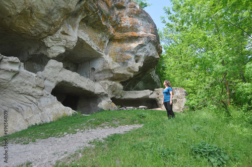 A woman stands near the Northern Caves of the cave city of Tepe-Kermen and looks at them. Bakhchisarai Historical, Cultural and Archaeological Museum-Reserve.