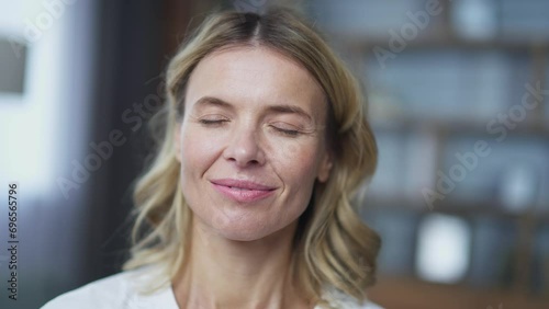 Close up face mature woman meditating with eyes closed sitting in lotus position on sofa in living room at home. Calm female in rest relaxes doing yoga breathing exercises after working day photo