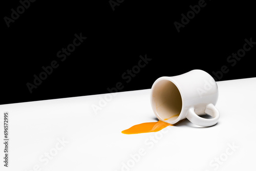 Creamed coffee spilling from a white restauraunt-style mug on a white table against a black background