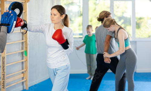Focused woman in boxing gloves practices punches with man in mitts in gym © JackF