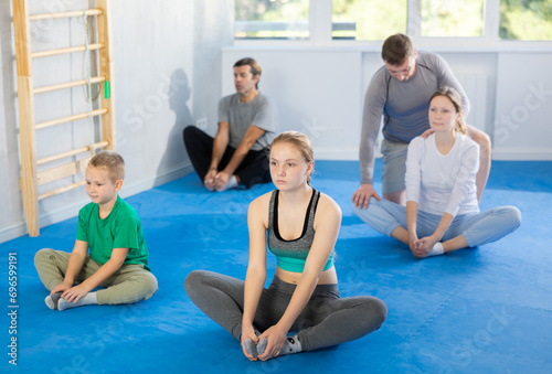 Cheerful family, parents with children athletes before training martial arts performs stretching butterfly exercise. Modern positive family chooses active hobby and leisure activity.