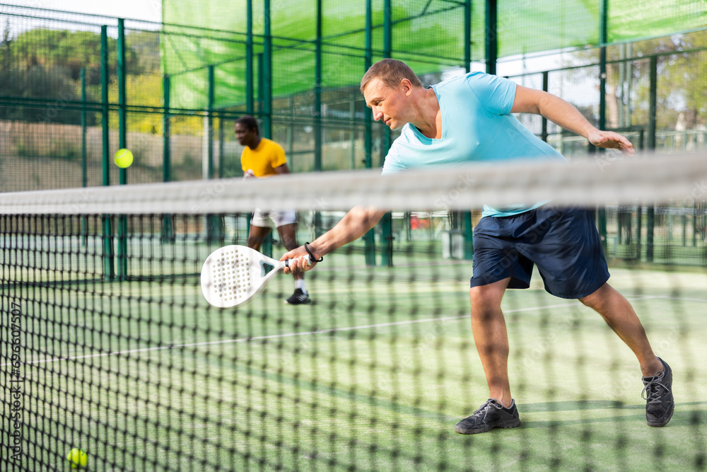 Sporty european man padel tennis player trains on the outdoor court using a racket to hit the ball