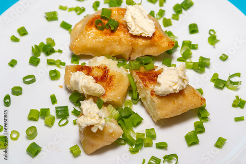 Fried pieroguis Ukrainian traditional food, on white plate on tablecloth decorated with typical Ukrainian embroidery. With cream and fresh chives in fine details. Prudentópolis PR photo