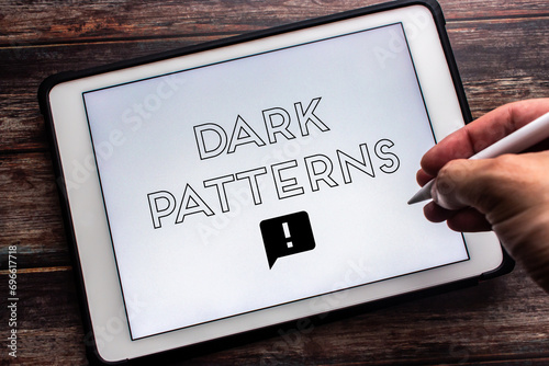 Keyword “Dark Patterns” seen on tablet on wooden table. Man hand holding wireless stylus pen. Deceptive online business practice concept photo