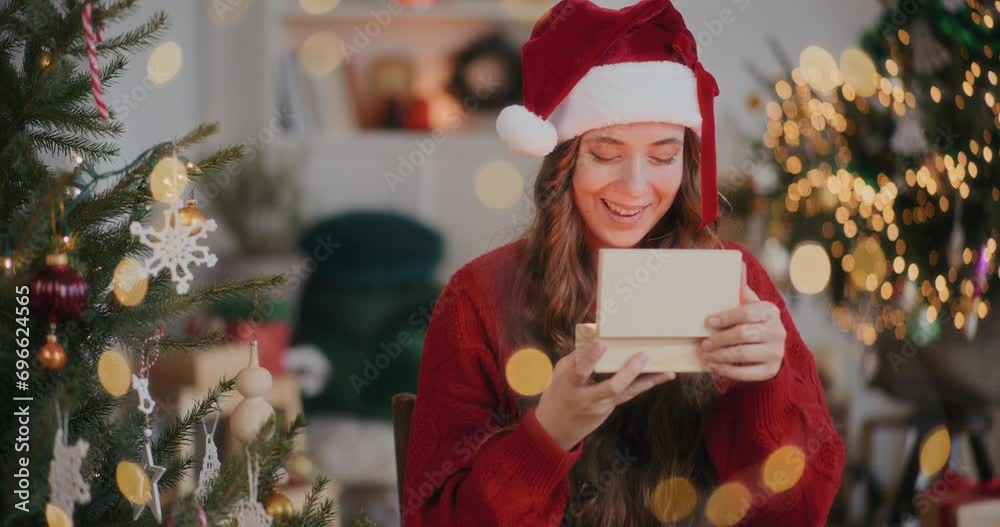 Amazed woman in Santa hat opening wooden gift box at decorated home Amazed woman in Santa hat opening wooden gift box at decorated home