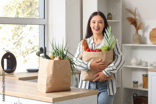 Young Asian woman with shopping bags full of fresh food at table in kitchen