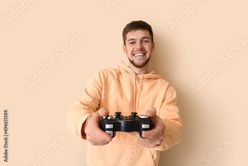 Young bearded man with game pad on beige background