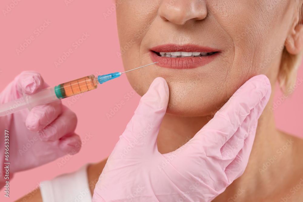 Beautiful mature woman receiving lip injection on pink background, closeup Beautiful mature woman receiving lip injection on pink background, closeup