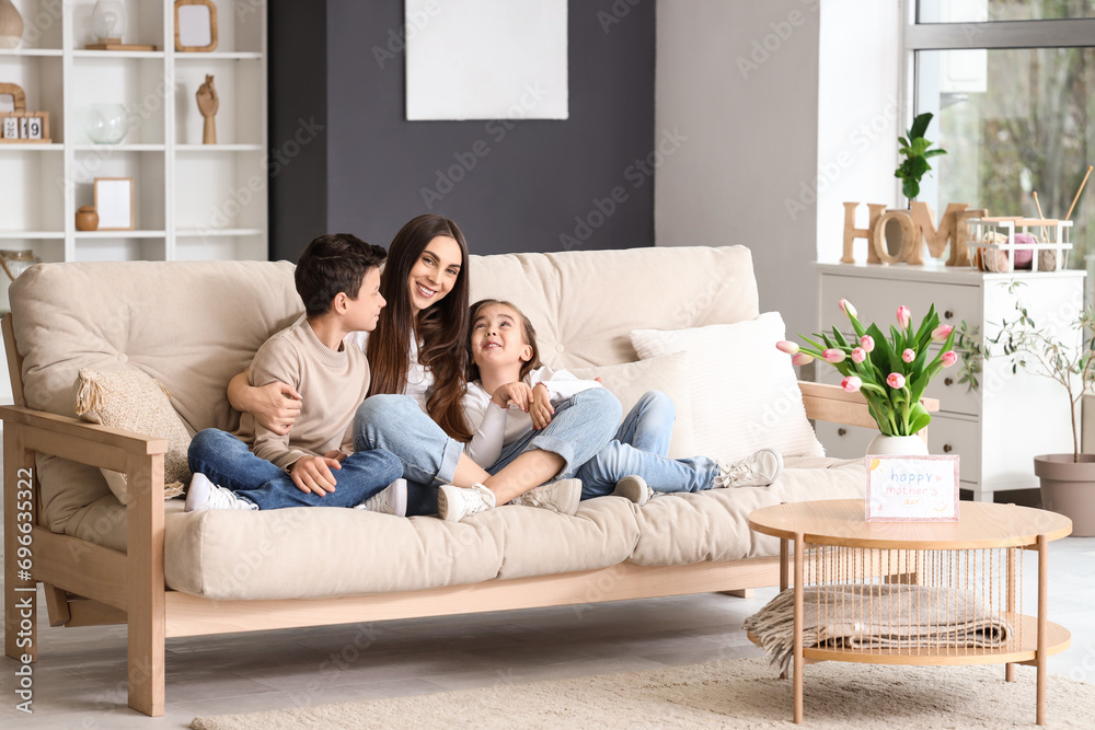 Young woman with her little children hugging on sofa at home. Mother's Day celebration Young woman with her little children hugging on sofa at home. Mother's Day celebration