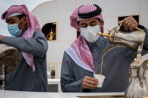 A young Qatari Arab in traditional dress pours Arabic coffee from the pot into the cup at Al Darab Saai at Umm Salal Mohamad in Doha, Qatar. During celebrate Qatar national day. photo